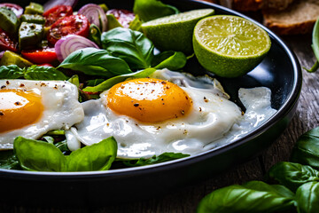 Sunny side up eggs with avocado, cherry tomatoes, toasted bread and red onion on wooden table

