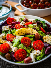 Fresh Greek salad - feta cheese, cherry tomatoes, artichokes, lettuce, black olives and onion on wooden table
