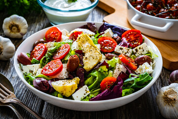 Fresh Greek salad - feta cheese, cherry tomatoes, artichokes, lettuce, black olives and onion on wooden table
