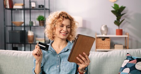 Internet banking, online shopping and technology concept. Portrait of happy smiling caucasian woman sitting on sofa with tablet pc computer and credit card at home. Woman enjoying of online shopping