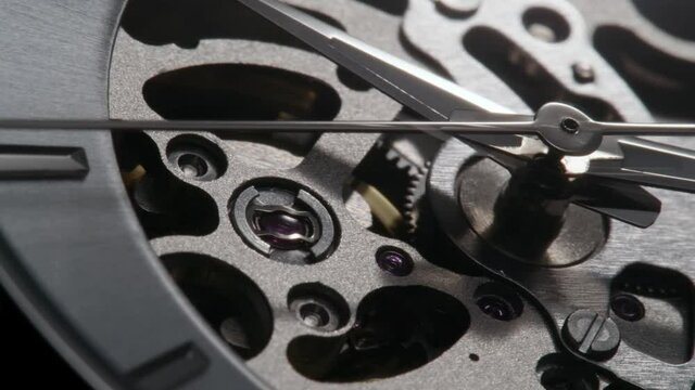 Second arrow running on the skeleton clockface. Metallic watch with open balance and mechanism turning around with the light flash