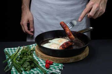 Scrambled eggs on a dark background. Fried eggs with fried sausages. Tasty breakfast. Unhealthy food.