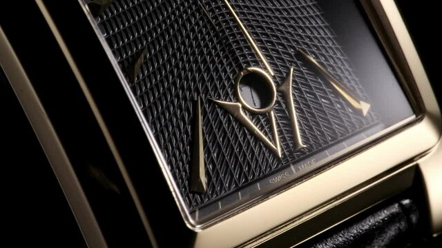 Second arrow is passing by the date and numbers on luxury golden swiss made watch with square body and waffle pattern on clockface. Closeup with zoom-in effect