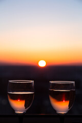 Two glasses with white wine on sunset background, evening sun is reflected in a misted glass. Concept of celebration, romantic date cocktail, love date, wine tasting