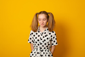 Obraz premium Shy child girl with two ponytails on a yellow background. Teenage girl is shy about her hairstyle.