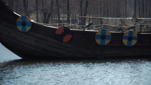 Drakkar floats on the river. Ancient Viking ship. A harsh journey in a historic ship along the river stream. Ancient sailors. Conquest campaigns. A warship with shields on board.