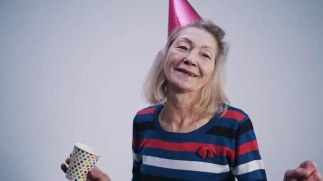Happy elderly woman with party hat and cup of drink dancing indoors. High quality 4k footage