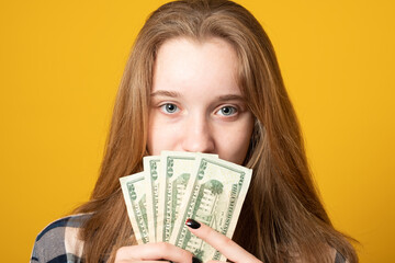 Close up portrait of a young girl holding money on a yellow background.