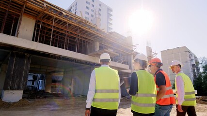 Multiethnic group of diverse specialists at construction site walking to the construction building to analyzing the plan of work - Powered by Adobe