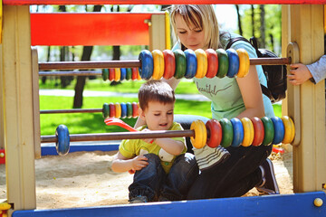 Fototapeta na wymiar Happy family concept. Mother and son are playing in the playground and laughing on a summer walk on a sunny day. Family holiday and togetherness, selective focus