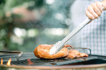 Man hand grilling barbecue on fire at backyard on day