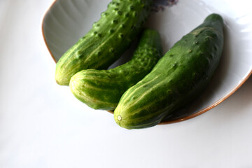 Three green cucumbers on a plate on a white background