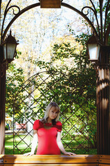 Portrait of young elegant cheerful woman with blonde hair sitting in autumn park in red dress. 