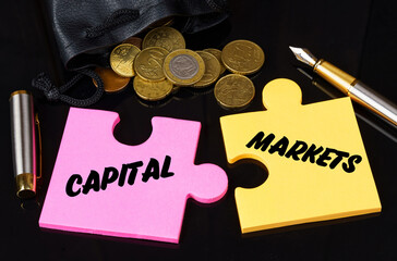 Coins are scattered on the black surface, there is a pen and puzzles on which it is written - CAPITAL MARKETS