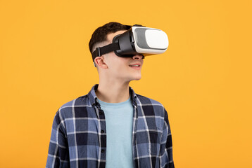 Cool guy in VR headset exploring cyberspace, using virtual reality for entertainment or studies on orange background