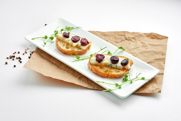 Appetizing italian antipasti - bruschetta with gorgonzola cheese and cherry, served on a white plate on a white plate