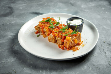 Traditional stuffed cabbage rolls with minced meat and rice stewed in tomato sauce in a white plate on a gray background. Ukrainian food