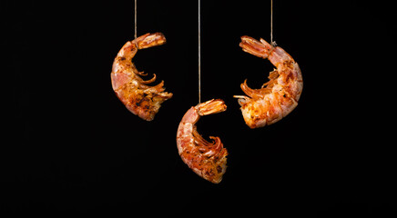 Obraz premium Fried shrimps hang on strings on a black background. Seafood appetizer, no people, horizontal orientation, copy space, close-up