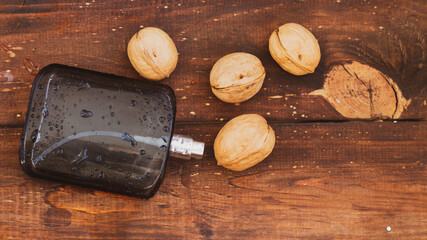 Fototapeta na wymiar Fragrance for men in a black spray bottle on a brown wooden background with walnuts in a hard shell