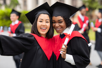 Cheerful young ladies in graduation robes taking selfie