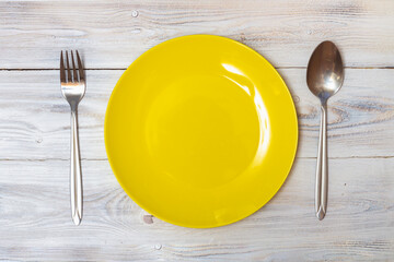 An empty yellow plate with a spoon and fork without food stands on a white table