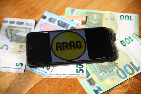 Leipzig, Germany - April 11, 2021: Closeup of smartphone with logo lettering of ARAG insurance company on paper money currency (selective focus on center of lettering)