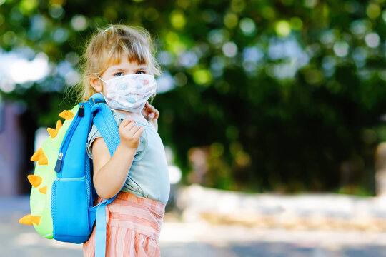 Little sad toddler girl with medical mask against corona virus covid on way to nursery or playschool. Unhappy upset child with disturbing mask. Kids with mental problems due coronavirus lockdown