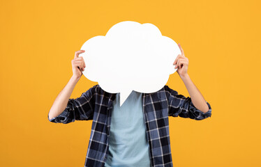 Unrecognizable young man holding blank speech bubble in front of his face over orange background,...