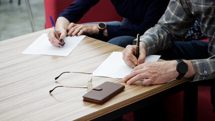 An adult woman and a man, sitting at a table in the office, fill out documents or forms. The...