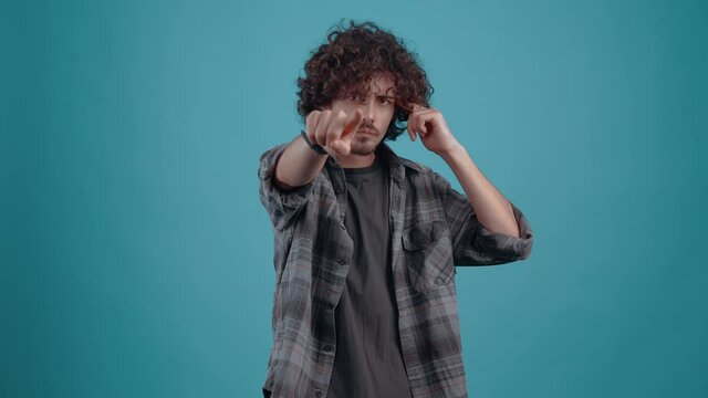 Young irritated hipster, points his finger in the face and shows the bad sign, in the studio on a turquoise background. The concept of people's lifestyle