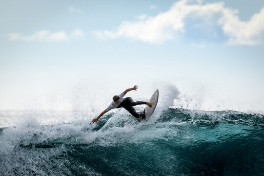 Young surfer with with wetsuit enjoying big waves in Tenerife, Canary Islands. Sporty boy riding his surf board on the ocean wave. Brave teenager making tricks on the rough sea during a competition.