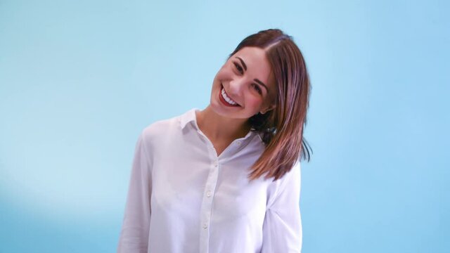 Beautiful caucasian woman with brown hair wearing white shirt dances against blue background. White teeth smile. 4K Resolution video.