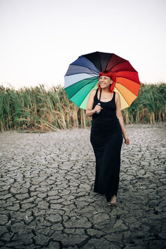 young woman with orange hair with a colorful umbrella on cracked earth