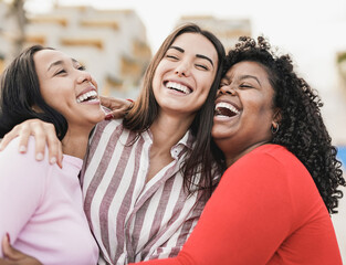 Happy latin women laughing and hugging each other outdoor in the city - Millennial girls and friendship concept - obrazy, fototapety, plakaty