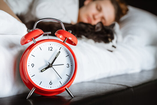 Young Millennial Candid Woman Sleeping With Pet Cat On White Blanket Bed Cozy At Home In The Bedroom. Close Up Of Alarm Clock, Morning Time, Wake Up, Female Healthy Lifestyle Concept.