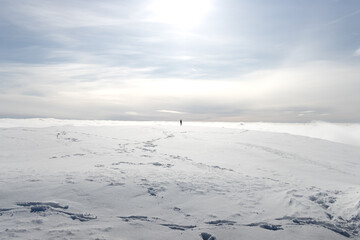 Obraz premium person walking alone on mountain above clouds in ski resort under the sun