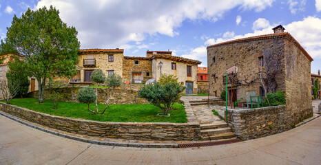 Obraz premium Panoramic of old stone houses with green garden and flowers and blue sky with clouds. Fisheye lens. La Hiruela Madrid.