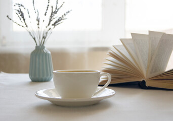 Still life with a cup of coffee and a book. The atmosphere of a cozy morning. Breakfast at home or in a cafe near the window