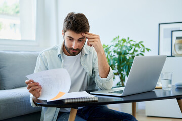 Worried young man looking on bills while at home
