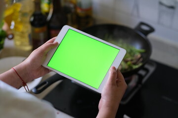 over shoulder view of woman holding green screen tablet when cooking in the kitchen