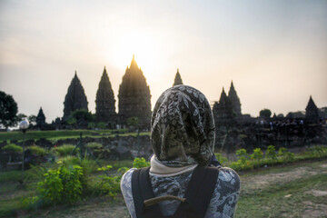 A young Asian muslim woman wearing hijab looking at the temple during sunset at the ancient Prambanan temple complex in Indonesia.
