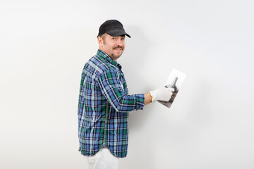 A builder in a black cap plastering a white wall with a knife for decorative plaster, putty