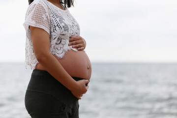 Pregnant woman in a blue dress on sea and sky blurred background.