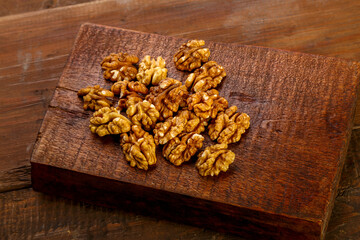 Fototapeta premium Walnuts sprinkled on a square board on a wooden table.