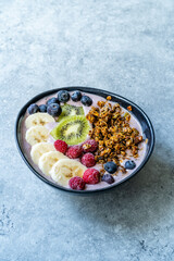 Acai Smoothie Bowl with Baked Granola, Blueberries, Raspberry, Banana and Kiwi in Hand.