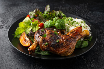 Slow cooked aromatic duck legs with basmati rice and side salad served with orange wedges on black plate