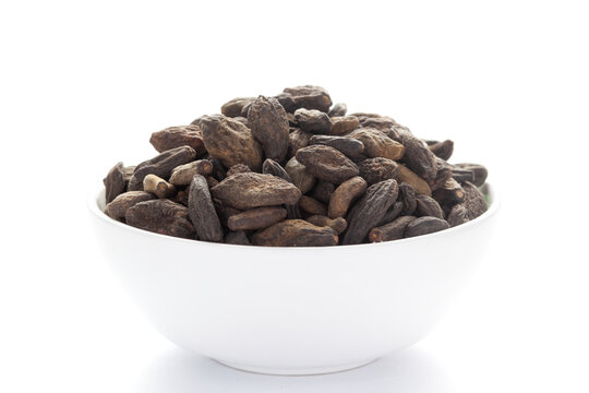 close-up of Organic Myrobalan or harad (Terminalia chebula) on a ceramic white bowl. Pile of Indian Aromatic Spice. 
