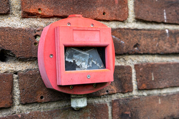 Hand fire alarm with broken glass on brick wall