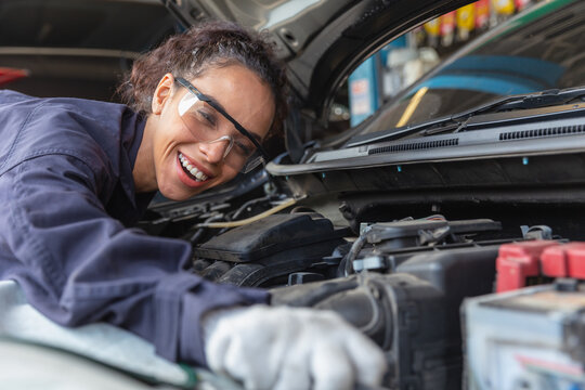 Woman Worker At Automobile Service Center, Female In Auto Mechanic Work In Garage Car Technician Service Check And Repair Customer Car, Inspecting Car Under Hood Battery Engine Oil Change