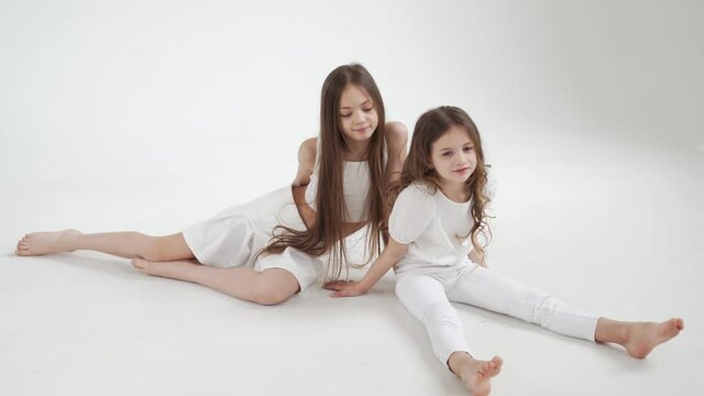 little girls with long hair in white clothes play, indulge and tickle each other
